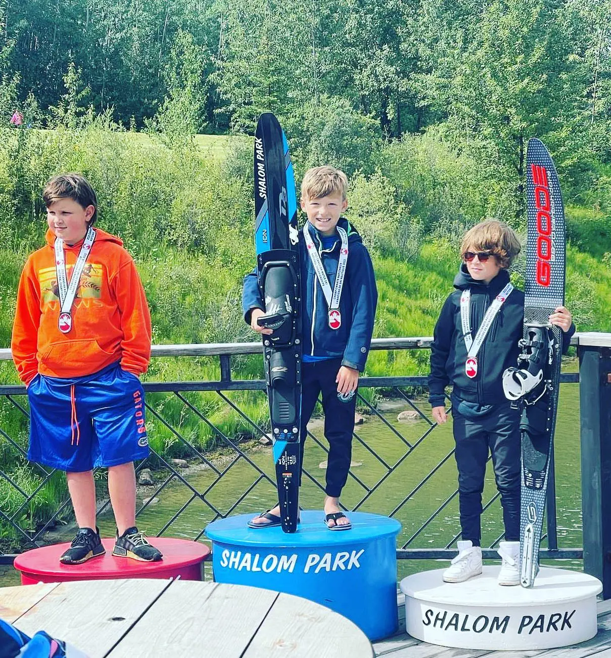 Three kids standing on a platform with skis.