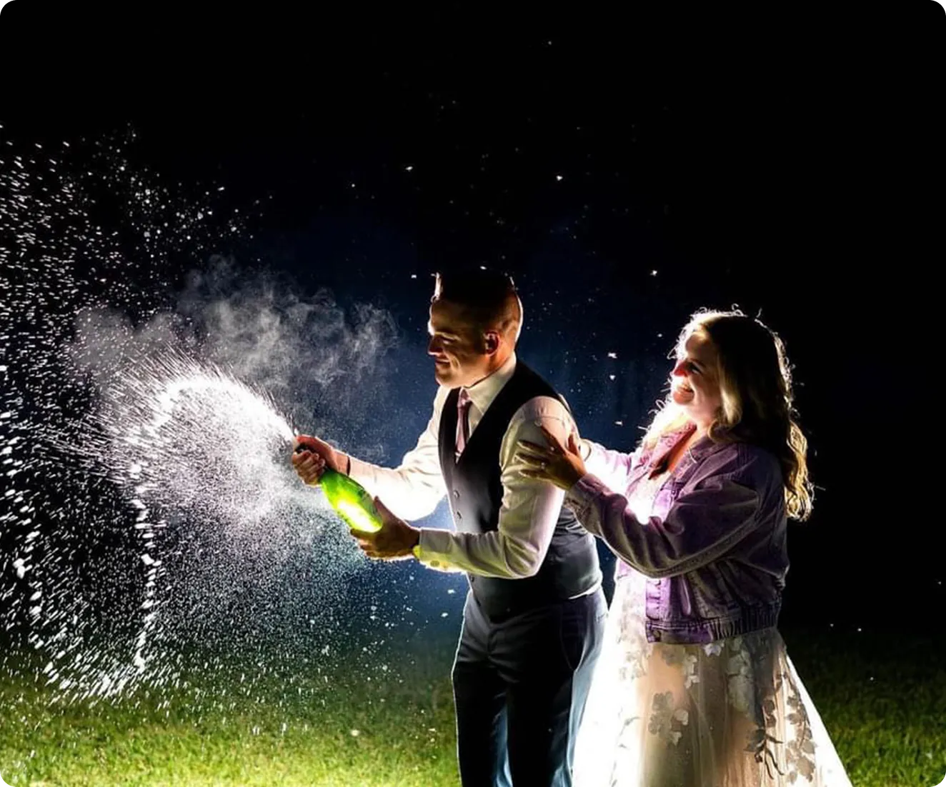 A man and woman spraying champagne in the dark.