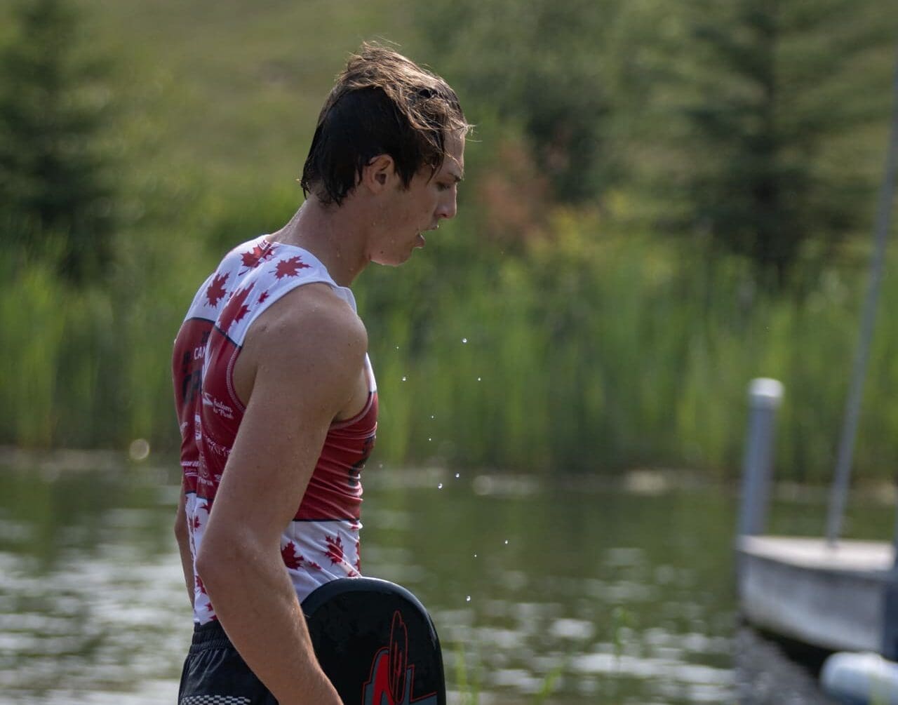 A man standing on the shore of a lake holding onto a paddle.