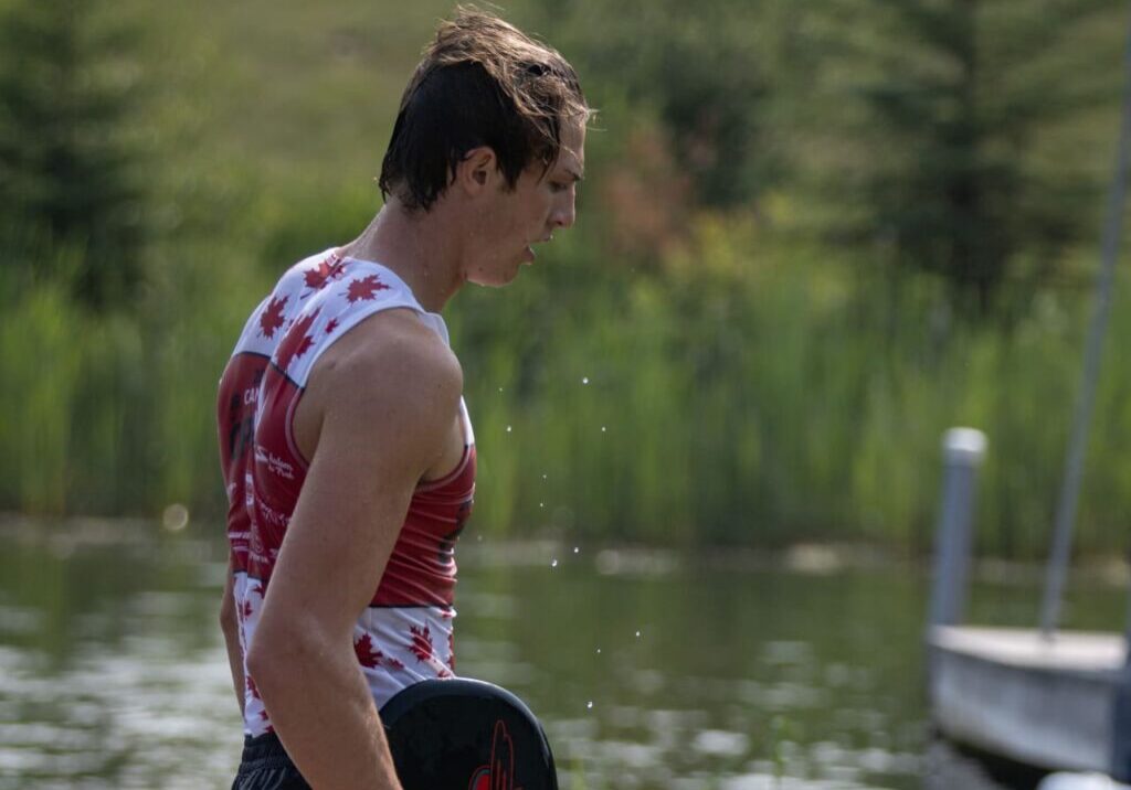 A man standing on the shore of a lake holding onto a paddle.